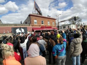 View from the back of a large crowd before the George Floyd Memorial, many with their fists or hands raised