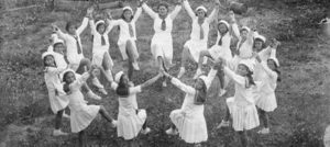 Image of jews, dressed in white, dancing with their hands together in a circle to celebrate Tu B'av, shown in black and white