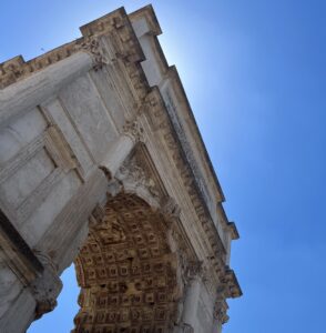 A photo of a roman archway, like the Arch of Titus, against a clear blue sky.