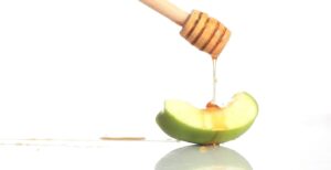 honey being drizzled on a wedge of granny smith apple.