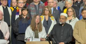 Rabbi Tamar Magill-Grimm speaking at a press conference. Cantors Tamar Havilio and Rachel Stock Spilker are behind Magill-Grimm to the right.